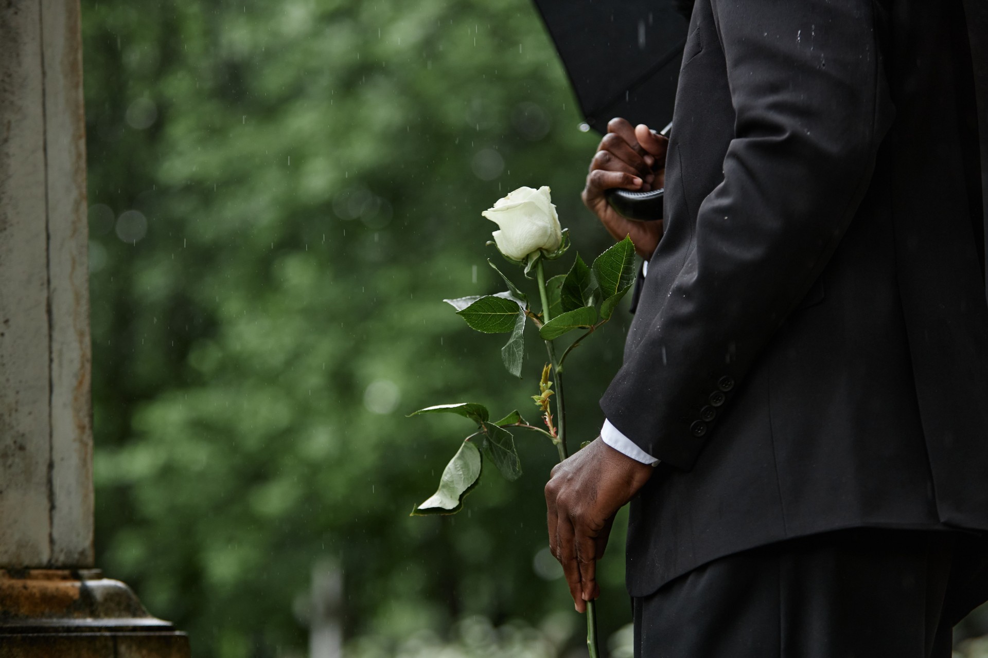 Un homme noir tenant une rose blanche avant de déposer une fleur sur la tombe d’un cimetière